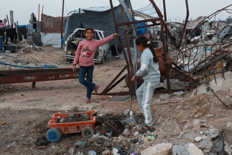 Children play beside the rubble and destroyed buildings in the Deir al-Balah area of central Gaza on February 20, 2026 [Abdelhakim Abu Riash/ Al Jazeera]